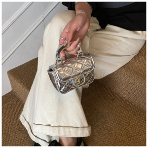 Detailed view of mini silver quilted handbag with golden twist lock held by a model