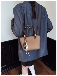 Detail of a brown canvas tote bag with leather straps and chocolate-shaped pendant charm
