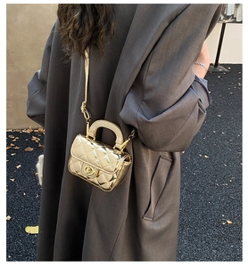 Close-up of golden quilted mini handbag with metal turn-lock and chain strap on a model