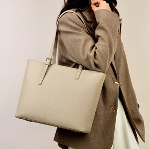 Chic cream leather tote bag with adjustable strap worn by model in a stylish blazer