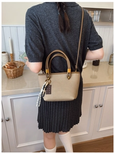 Detail of khaki textured crossbody bag with leather trim and chocolate charm