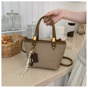Detail of khaki fabric tote bag featuring brown leather trim and chocolate shaped charm