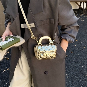 Macro detail of a mini gold quilted bag with metallic texture and rotary lock on gray blazer