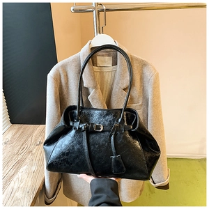 Detail of a large black waxed leather shoulder bag featuring a stylish buckle and charm