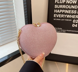 Detail of pink heart-shaped evening bag with glitter texture and gold double heart zippers
