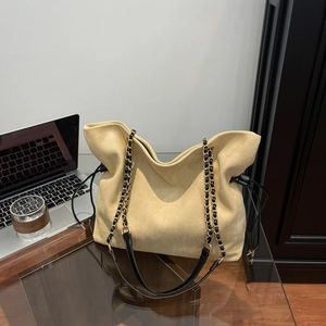 Beige suede drawstring tote bag with black leather chain straps on office desk