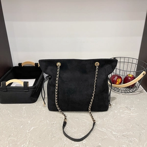 Minimalist black suede drawstring tote bag with gold chain strap in a lifestyle setting