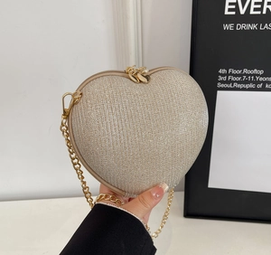 Macro detail of heart-shaped evening bag with champagne glitter finish and gold chain