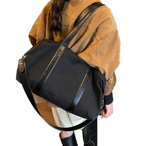 Minimalist black canvas travel bag with polished leather handles and wide shoulder strap