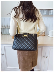 Détail d'un sac matelassé noir avec chaîne dorée porté par un mannequin femme