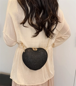 Detail of a black glitter heart-shaped crossbody bag with a gold chain on a beige outfit
