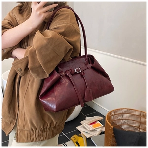 Detail of vintage burgundy leather tote bag with belt buckle and polished oil-wax texture
