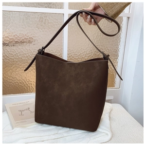 Close-up of a matte dark coffee bucket bag on white knit fabric with a leather strap
