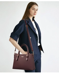 Detail of burgundy textured leather tote bag with gold hardware and logo on deep red surface