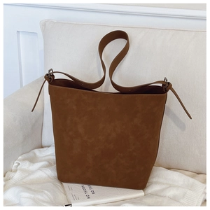 Brown frosted suede bucket bag with adjustable strap on a minimalist cream sofa