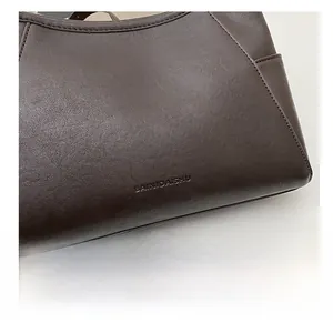 Detail of dark brown leather texture with embossed BAINIDAISHU logo on shoulder bag