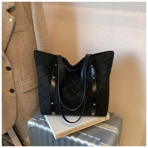Close-up of black quilted tote bag with silver studs on a silver suitcase
