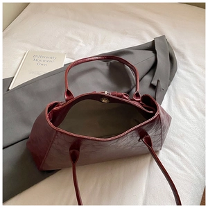 Close-up of burgundy patent leather tote bag with magnetic snap and textured finish