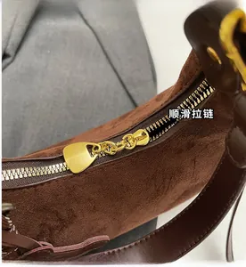 Detailed close-up of the smooth gold metal zipper on a dark brown suede handbag