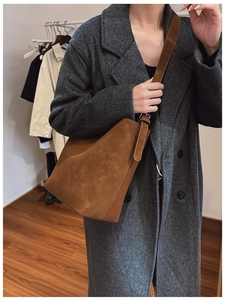 Close-up of a brown matte leather bucket bag worn by a model in a dark wool coat