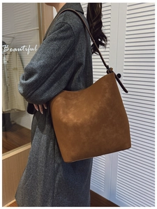 Brown matte bucket bag with adjustable strap worn on shoulder with grey tweed coat