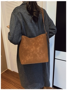 Brown frosted leather bucket bag worn over a grey coat, showing casual style and scale