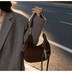 Detail of dark brown suede hobo bag with a leather bear charm and gold-tone hardware