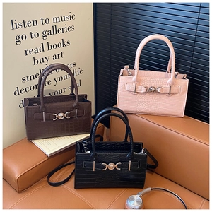Three crocodile pattern Kelly style bags in black, brown and pink on a stylish sofa