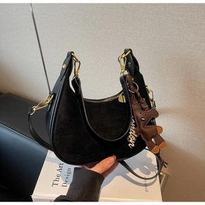 Detail of a black suede hobo bag with a brown bear charm and golden zipper hardware