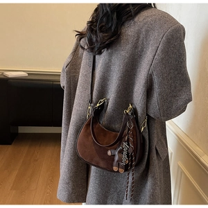 Detailed close-up of brown suede hobo bag with teddy bear charm on grey coat