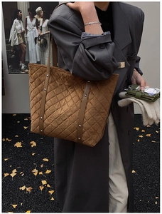 Close-up of brown quilted suede tote bag with silver studs on autumn leaf background