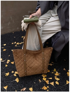 Detailed shot of brown quilted tote bag with silver rivets on autumn ginkgo leaves