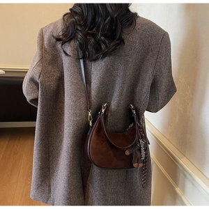 Detail of a brown crescent bag with suede texture and a London teddy bear charm