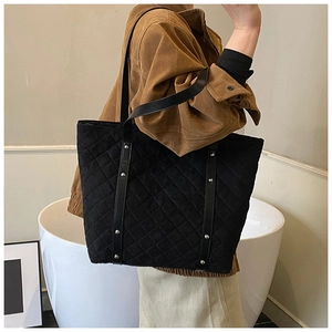Detail of black quilted tote bag with silver studs and double shoulder straps on model