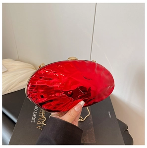 Close-up of red metallic acrylic shell clutch bag with gold chain on vintage books