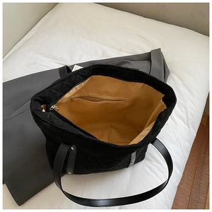 Detailed interior of a black quilted tote bag featuring a spacious yellow lining and zip pocket