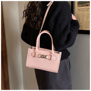 Detailed view of pink crocodile-embossed handbag with round metal clasp on a model shoulder