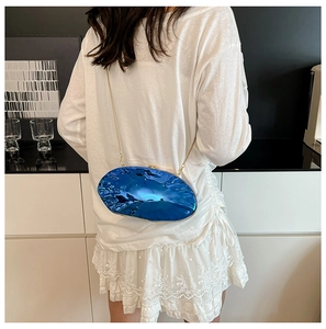 Detail view of blue rippled mirror clutch bag with a slim gold chain strap on person