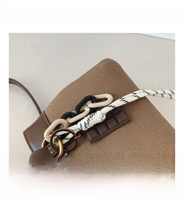 Close-up of brown leather bucket bag with metallic lock, resin chains and decorative charm