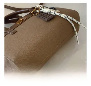 Detail of brown textured fabric bucket bag with leather handle and chocolate charm