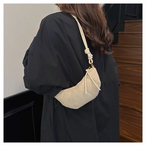Dettaglio borsa a mezzaluna beige con tracolla annodata su un cappotto nero chic