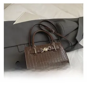 Detail of dark brown crocodile pattern bag with golden heart buckle on a white bed