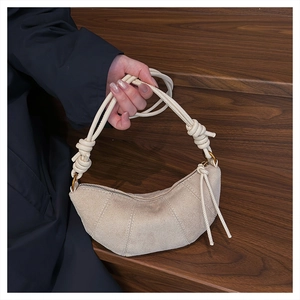Dettaglio della borsa croissant beige con manico a nodo e anello su scale scure