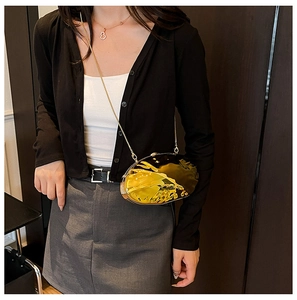 Model wearing a gold oval metallic clutch bag with a sleek fluid texture and chain strap