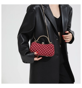 Detail of red polka dot handbag with gold metal handle and chain on black leather outfit