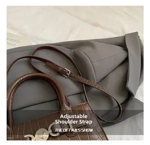 Close-up of heart-shaped metal lock and adjustable strap on brown crocodile pattern bag