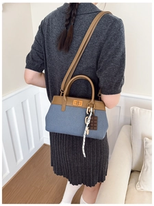 Detail of blue denim and brown leather handbag with gold twist lock and charm