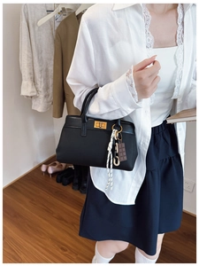 Detail of black leather handbag with gold metal clasp and woven handle charm decoration