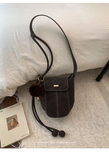Detailed view of brown suede bucket bag featuring contrast stitching and a fur pom charm