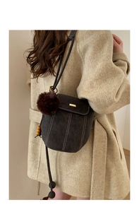 Close-up of suede bucket bag with white stitching, brown pompom, and gold buckle detail